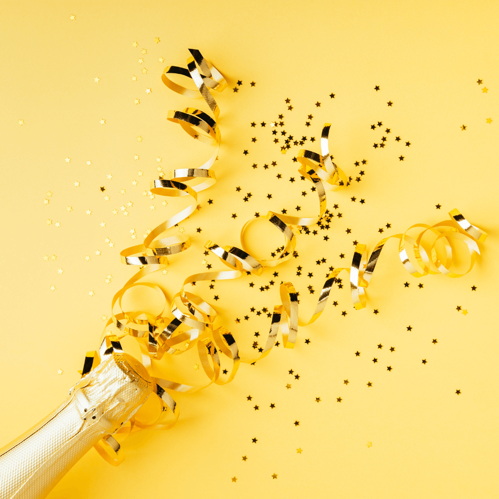 Champagnefles wat popt. Er komen glitters, snippers en serpentine uit. Gele achtergrond.