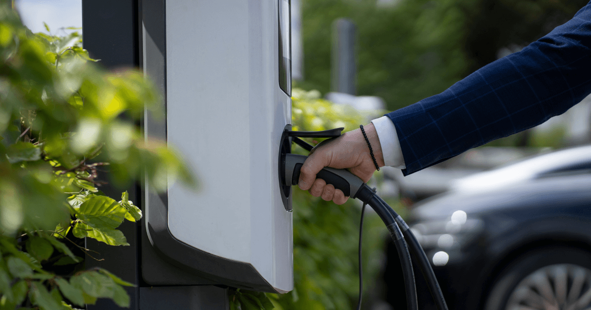 Hand aheeft laadkabel vast. Op de achtergrond staat een auto.
