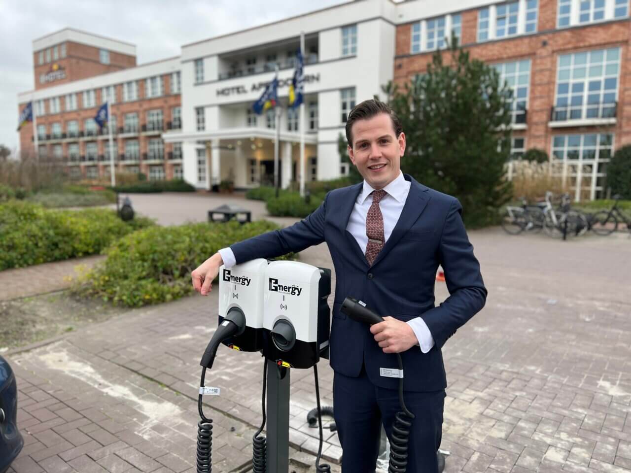 Thijs houdt een laadkabel vast en leunt over een laadpaal bij Van der Valk Apeldoorn.