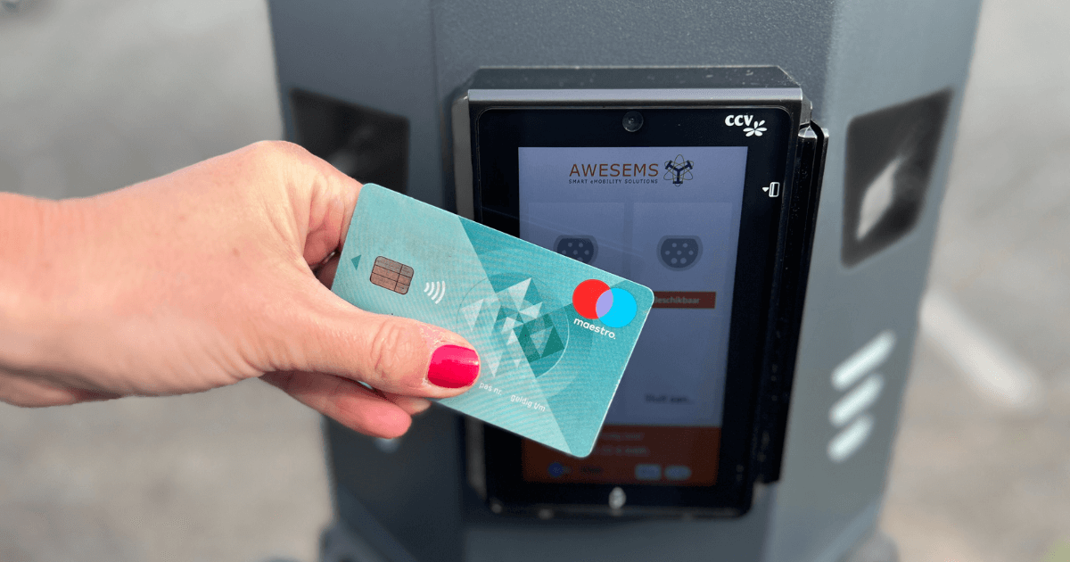 Een vrouwelijke hand heeft een pinpas vast. Deze houdt zij voor de pinterminal op een Awesems laadpaal.